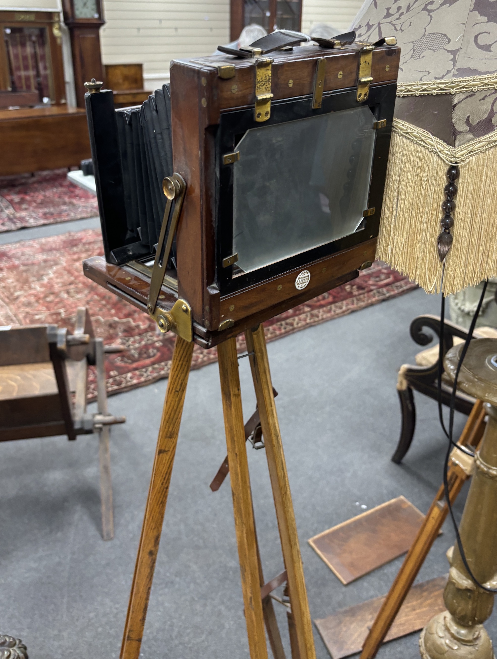 An early 20th century brass and mahogany ‘Challenge’ half plate bellows camera by J. Lizars, Glasgow, with a lens, and on an oak tripod